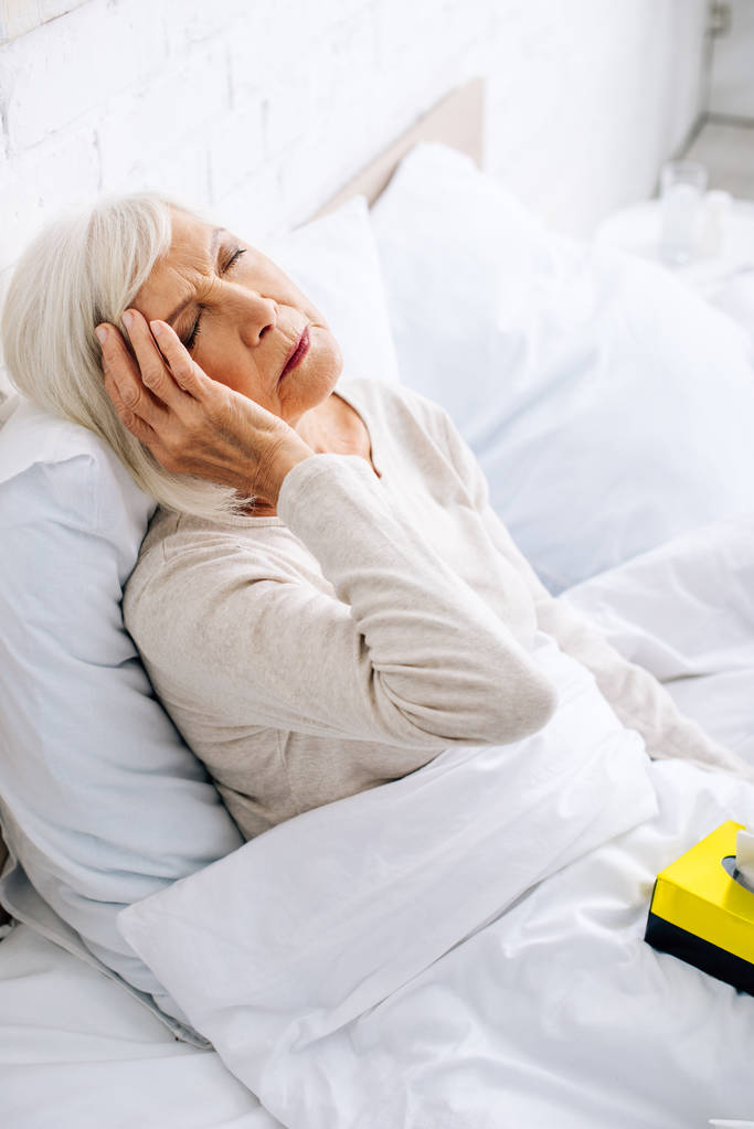 άποψη υψηλής γωνίας της άρρωστης ηλικιωμένης γυναίκας που έχει πονοκέφαλο στο κρεβάτι  - Φωτογραφία, εικόνα