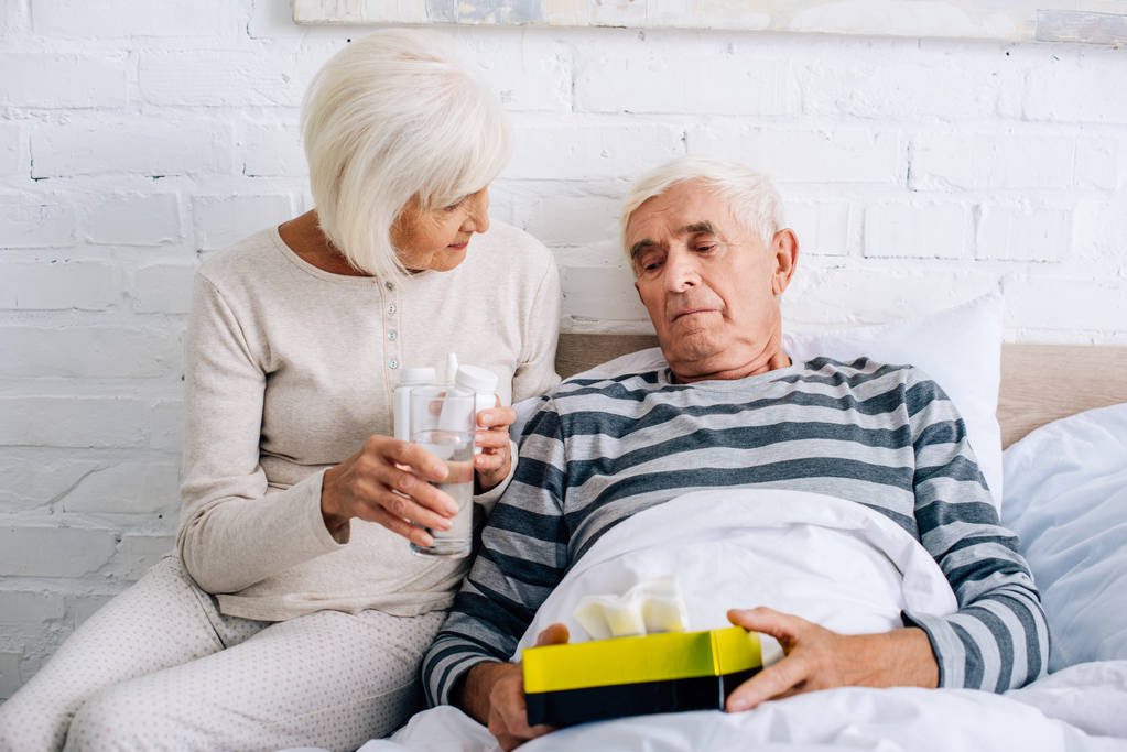 жена дает стакан воды больному мужу в постели
  - Фото, изображение
