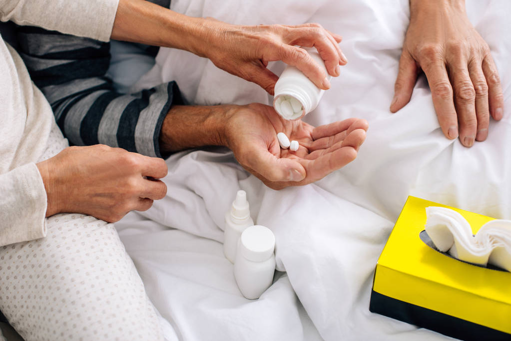 abgeschnittene Ansicht der Frau, die ihrem kranken Mann im Bett Tabletten verabreicht  - Foto, Bild