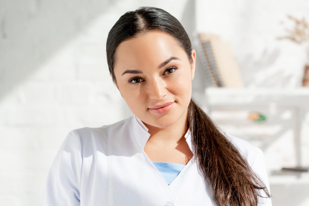 attractive and smiling dermatologist looking at camera in clinic  - Photo, Image