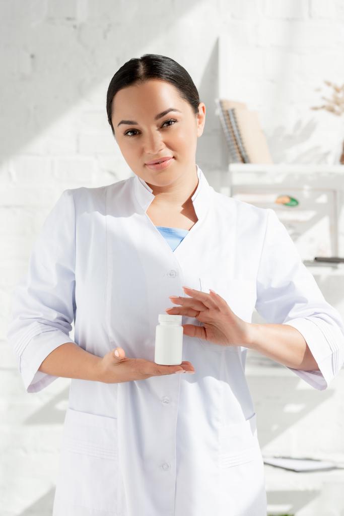 dermatologue attrayant en manteau blanc tenant bouteille avec des pilules en clinique
  - Photo, image