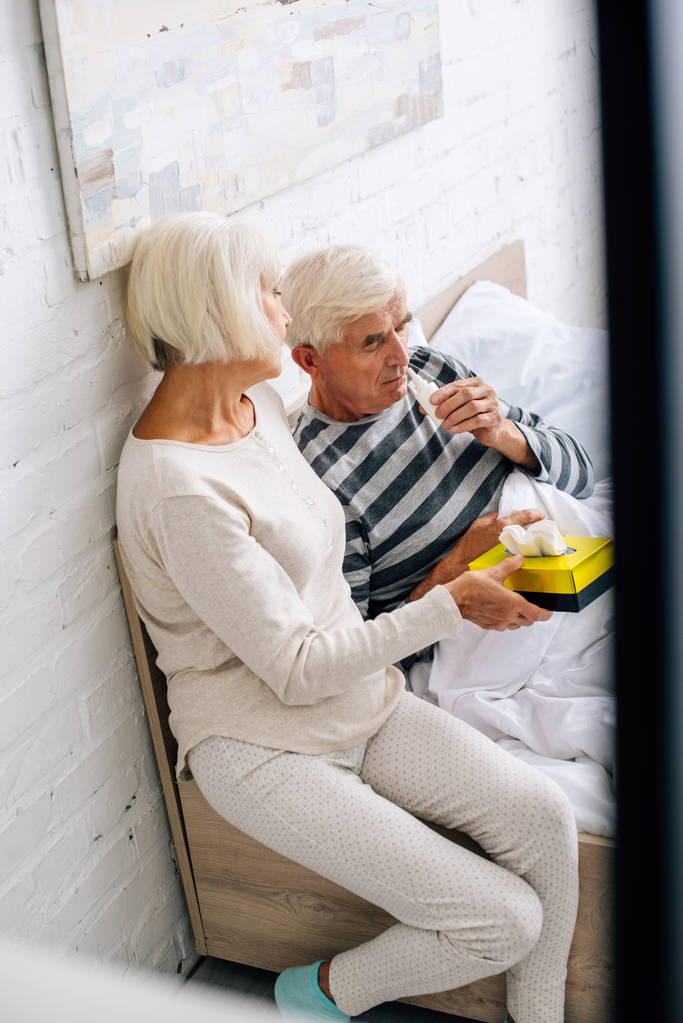 Hochwinkelaufnahme des Mannes mit Nasentropfen und der Frau mit Servietten in der Wohnung  - Foto, Bild