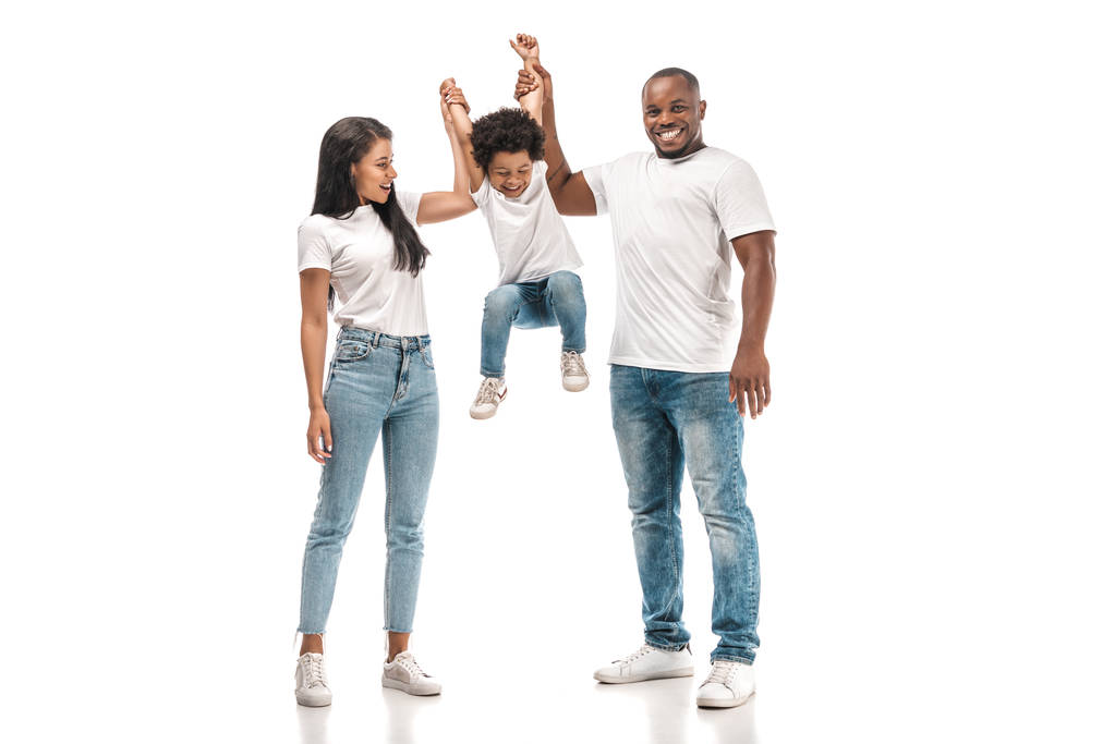 wesoły afrykański chłopiec wiszący na rękach rodziców na białym tle - Zdjęcie, obraz
