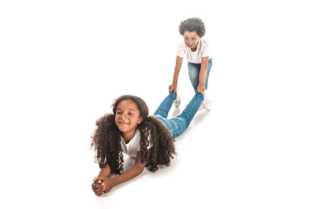 alegre afroamericano chico arrastrando hermana por piernas en blanco fondo
 - Foto, Imagen