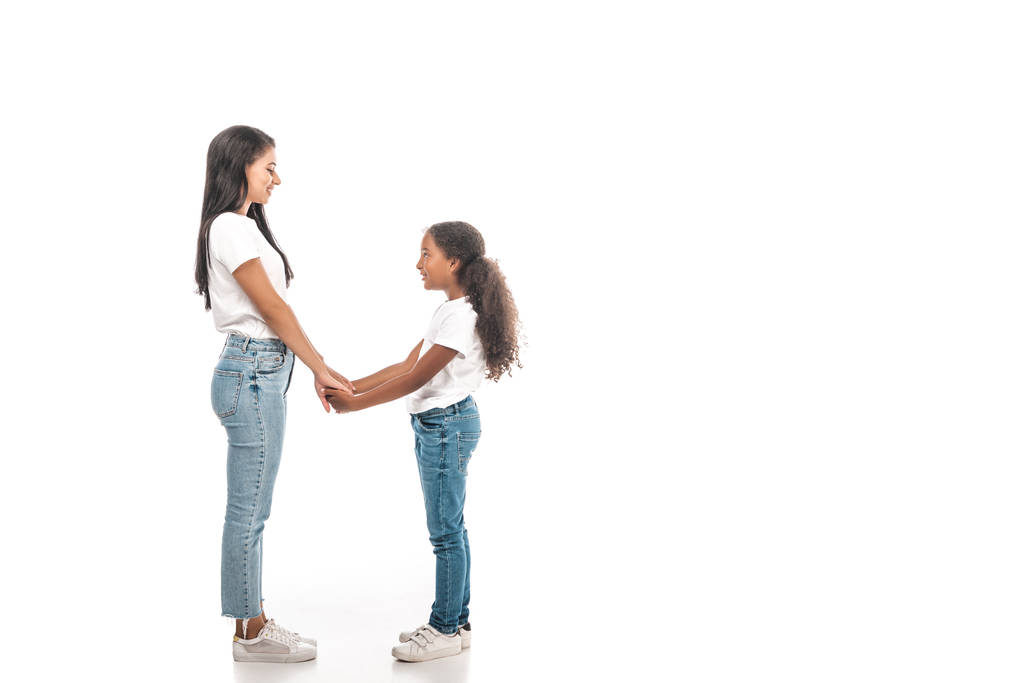 vista lateral de feliz afro-americana mãe e filha de mãos dadas e olhando uns para os outros no fundo branco
 - Foto, Imagem
