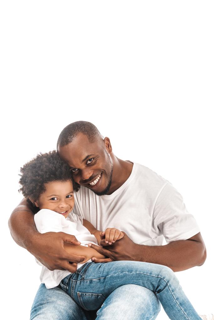 Χαρούμενος Αφροαμερικάνος που αγκαλιάζει τον αξιολάτρευτο γιο του και κοιτάζει την κάμερα απομονωμένη στα λευκά - Φωτογραφία, εικόνα