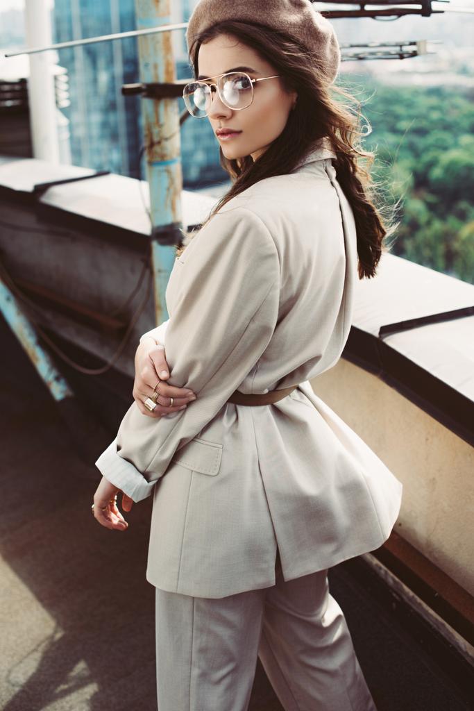 atraktivní módní model pózující v béžovém obleku a baretu na městské střeše - Fotografie, Obrázek