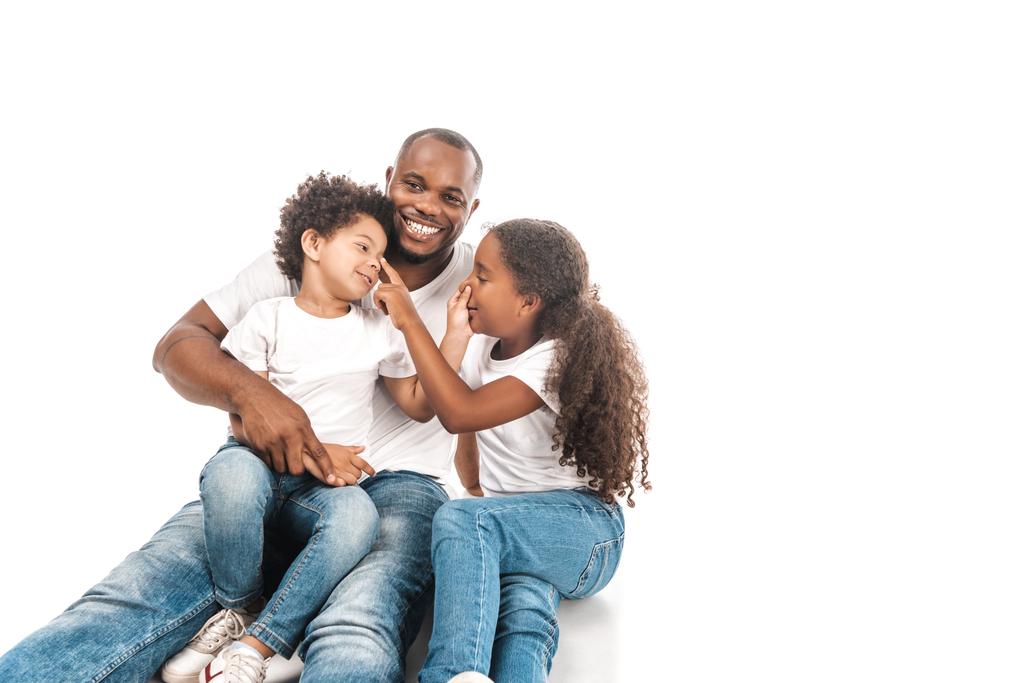 cheerful african american brother and sister touching noses of each other while sitting with dad on white background - Photo, Image