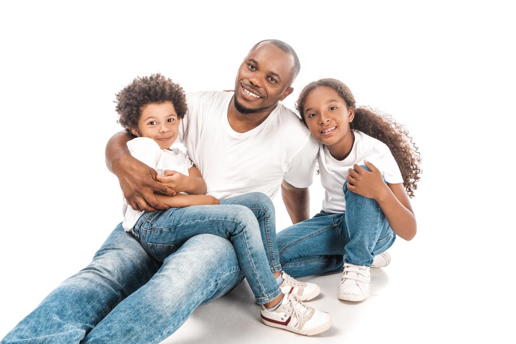 gelukkig Afrikaans amerikaanse man omarmen zoon en dochter terwijl zitten samen op witte achtergrond - Foto, afbeelding
