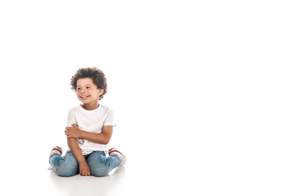 веселий афроамериканський хлопчик, дивлячись далеко, сидячи на білому тлі
 - Фото, зображення