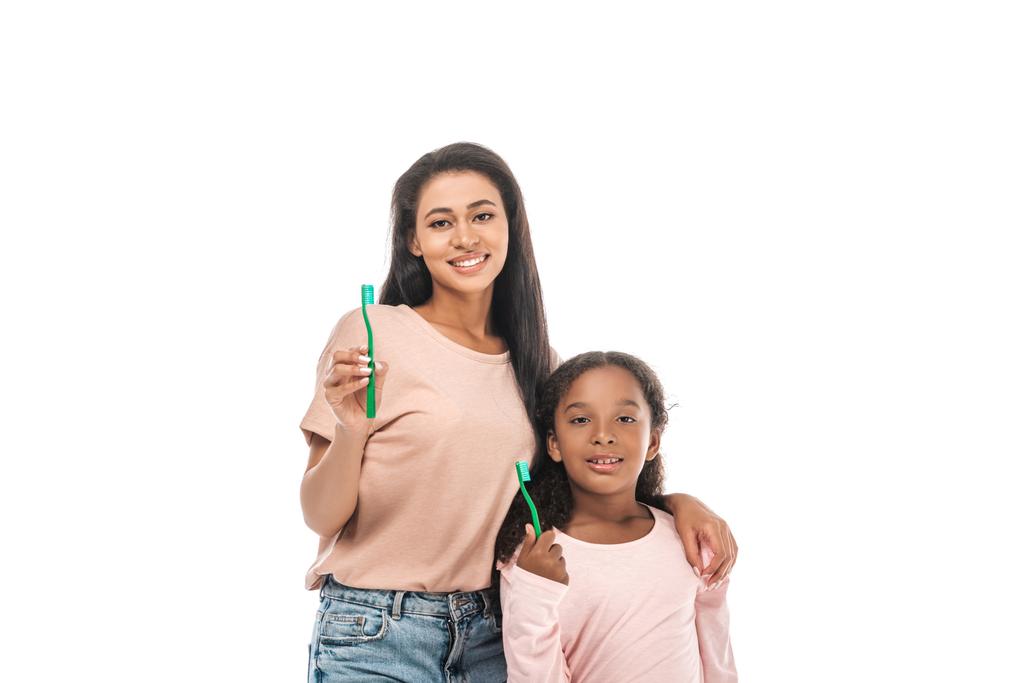 cheerful african american mother and daughter holding toothbrushes and smiling at camera isolated on white - Photo, Image