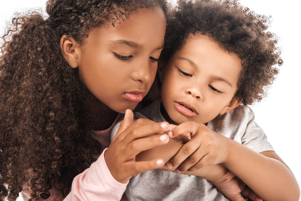 atenta hermana afroamericana mirando a mano de adorable hermano aislado en blanco
 - Foto, Imagen