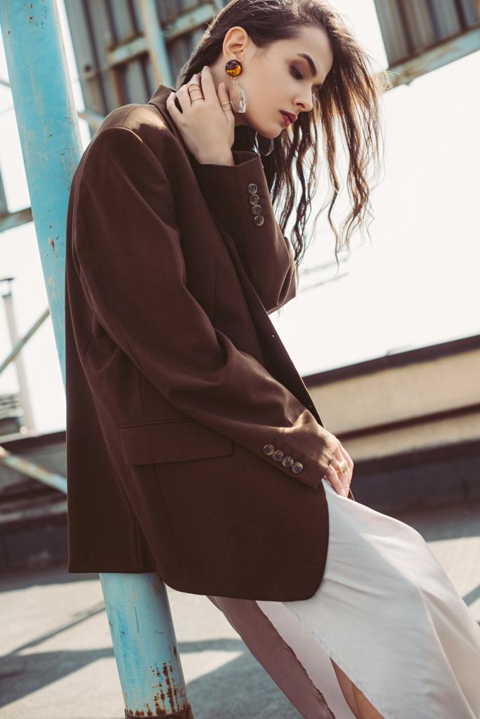 стильная девушка позирует в шелковом платье и коричневой куртке на крыше
 - Фото, изображение