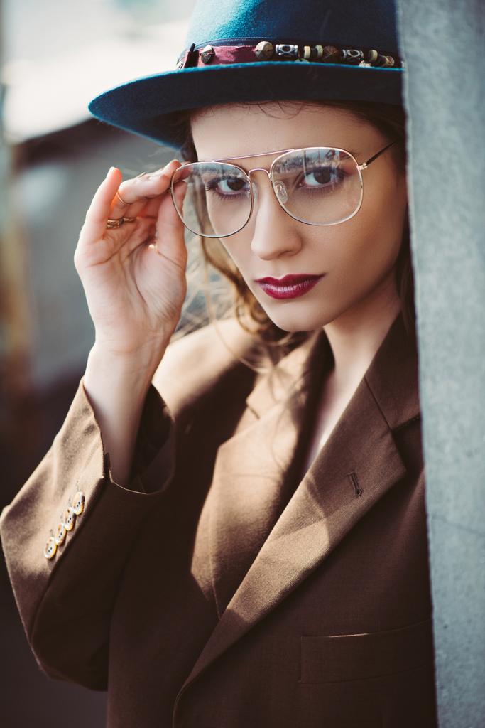 divatos elegáns nő pózol kalap, szemüveg és barna kabát a tetőn - Fotó, kép