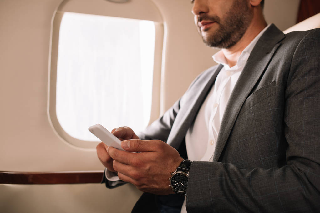 vista ritagliata di uomo d'affari barbuto utilizzando smartphone in jet privato
  - Foto, immagini