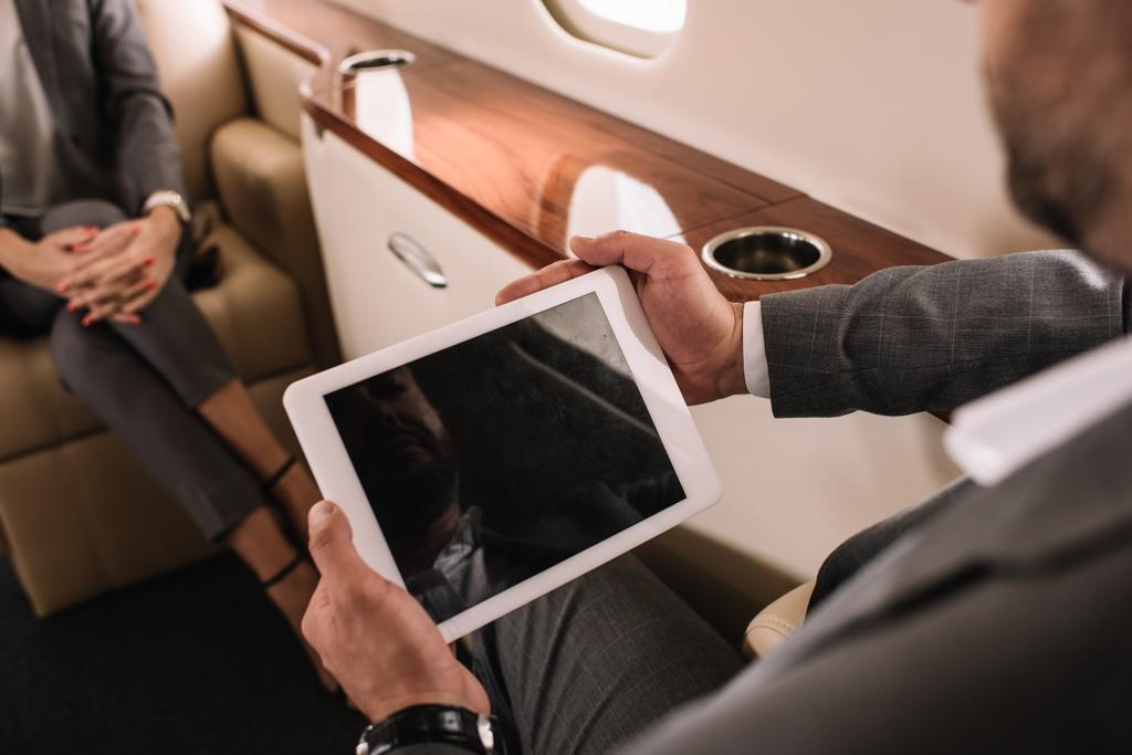 vista recortada de empresario sosteniendo tableta digital con pantalla en blanco cerca de compañero de trabajo en jet privado
  - Foto, imagen