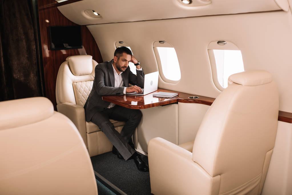 selective focus of bearded businessman using laptop in private jet  - Photo, Image