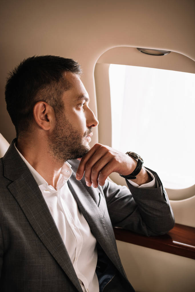 handsome bearded businessman looking at airplane window in private jet  - 写真・画像