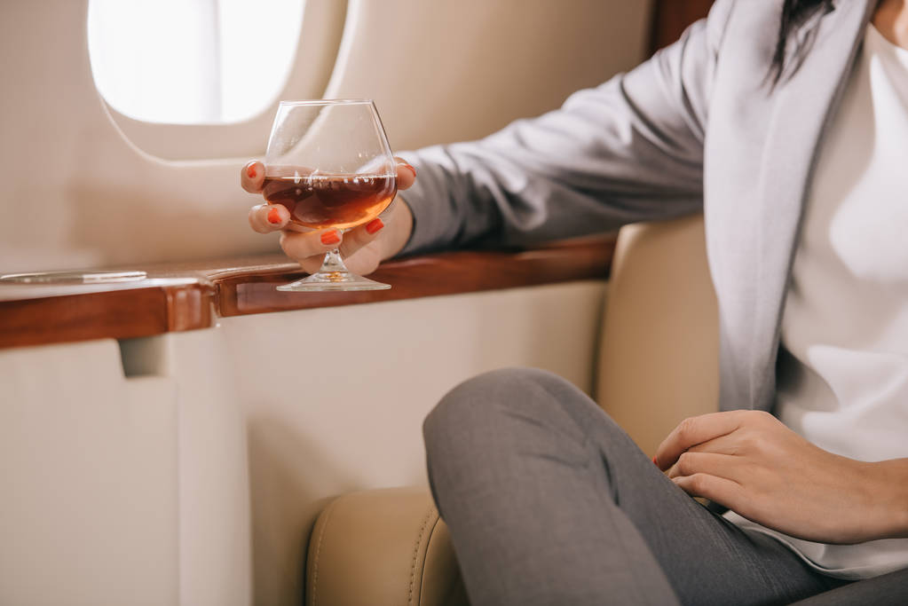 cropped view of businesswoman holding glass with cognac in private jet  - Photo, Image