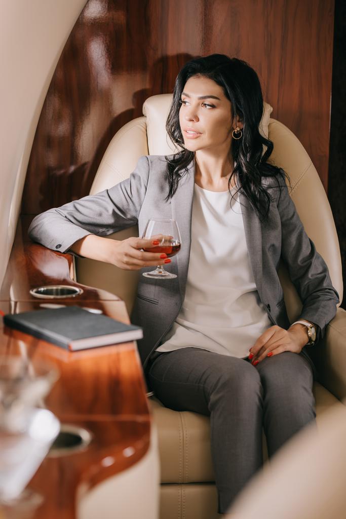 selectieve focus van zakenvrouw in formeel glas met cognac in prive jet  - Foto, afbeelding
