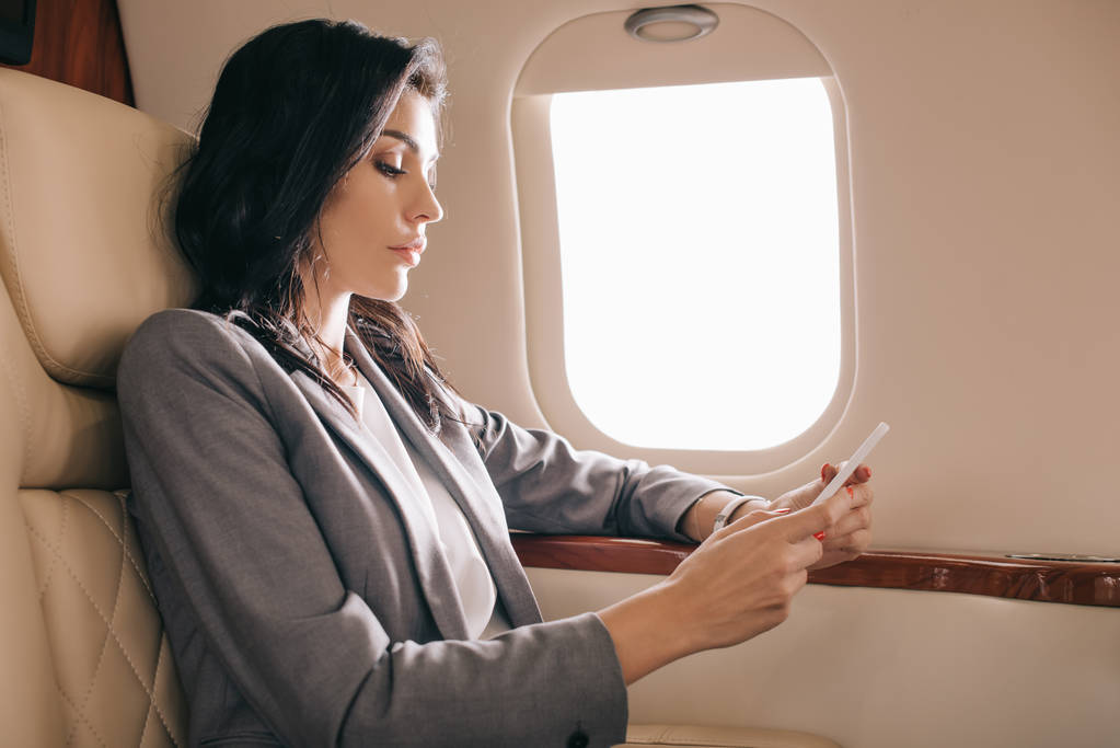 боковой вид бизнесвумен, использующей смартфон в частном самолете
  - Фото, изображение