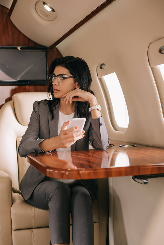 вибірковий фокус ділової жінки в окулярах за допомогою смартфона в приватному літаку
  - Фото, зображення