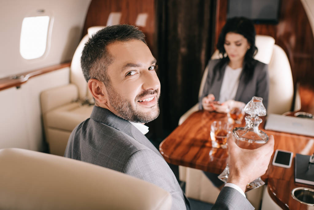 избирательный фокус счастливого бизнесмена, держащего банку с алкогольным напитком рядом с бизнесвумен в частном самолете
  - Фото, изображение