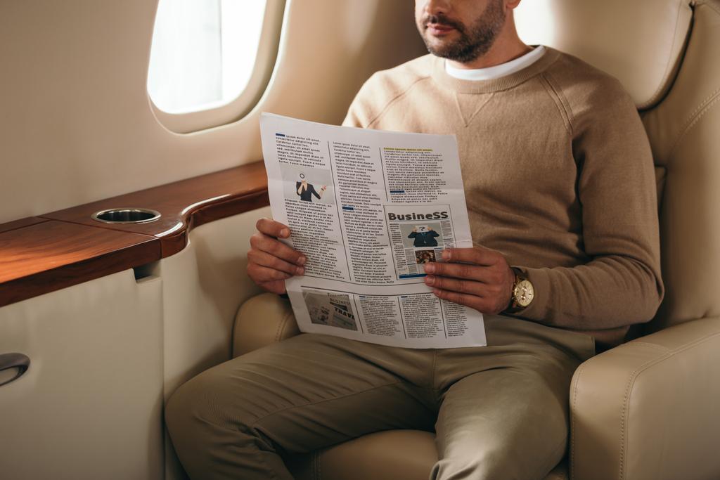 ostříhaný pohled na vousatého muže držícího noviny v soukromém tryskáči  - Fotografie, Obrázek