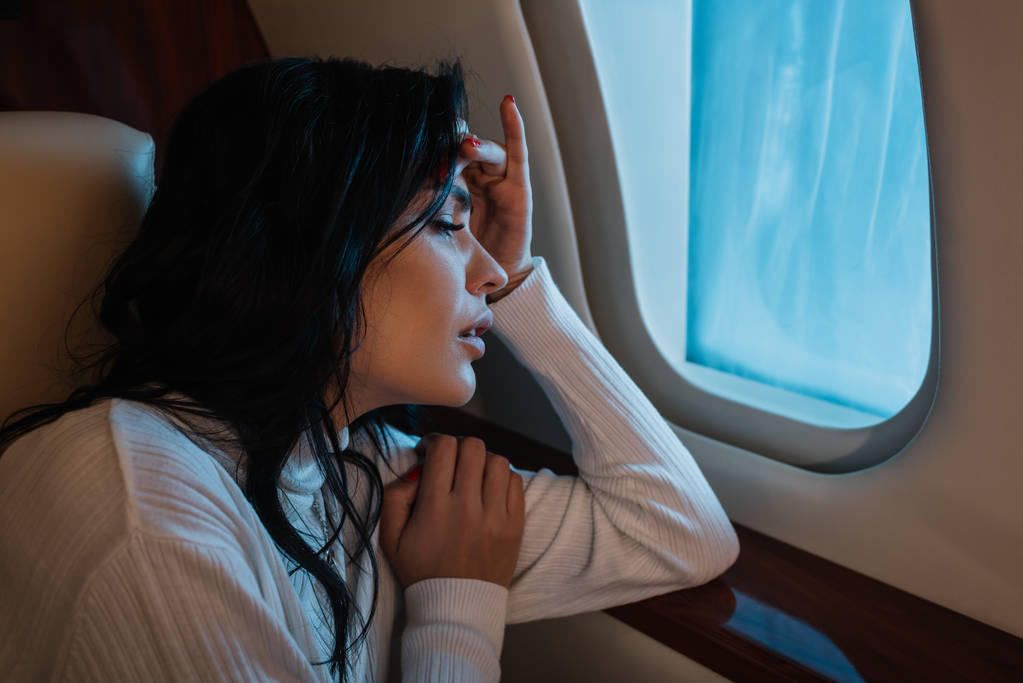 scared woman with airsickness looking at airplane window in private jet  - Photo, Image
