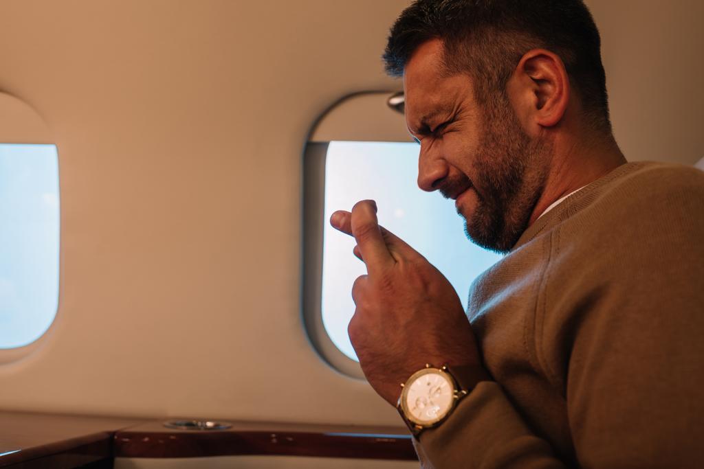 hombre asustado con los ojos cerrados y los dedos cruzados en jet privado
  - Foto, Imagen