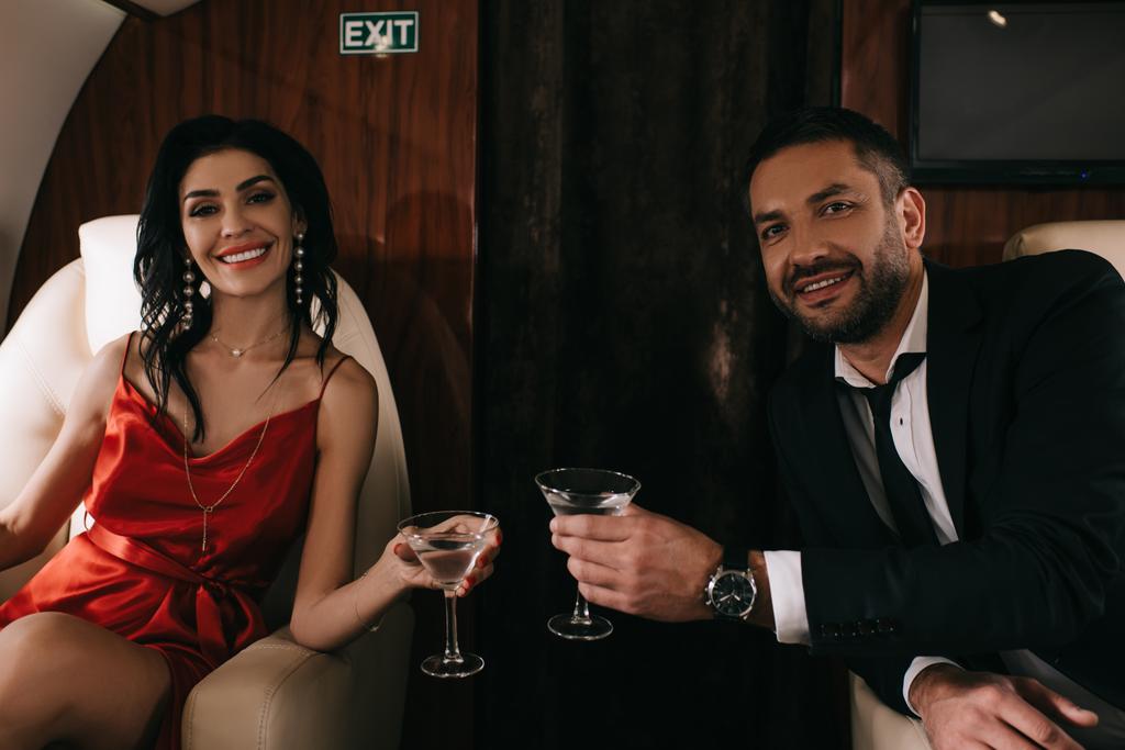 glücklicher Mann und Frau im roten Kleid mit Martini-Brille im Privatjet  - Foto, Bild
