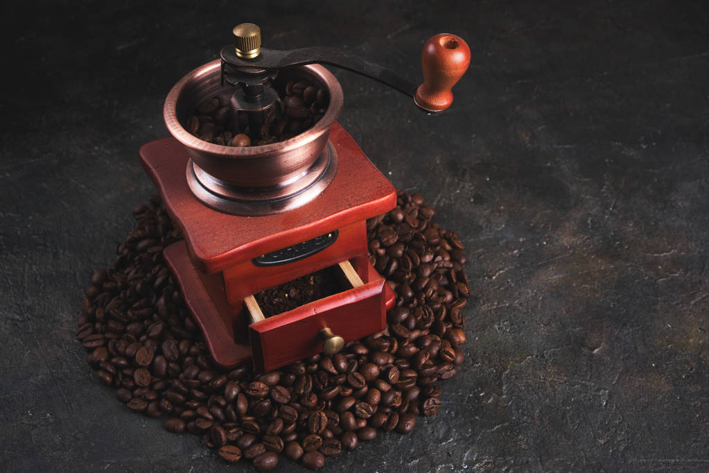 Molinillo de café viejo, lleno de granos de café, entre granos de café en concreto
. - Foto, Imagen