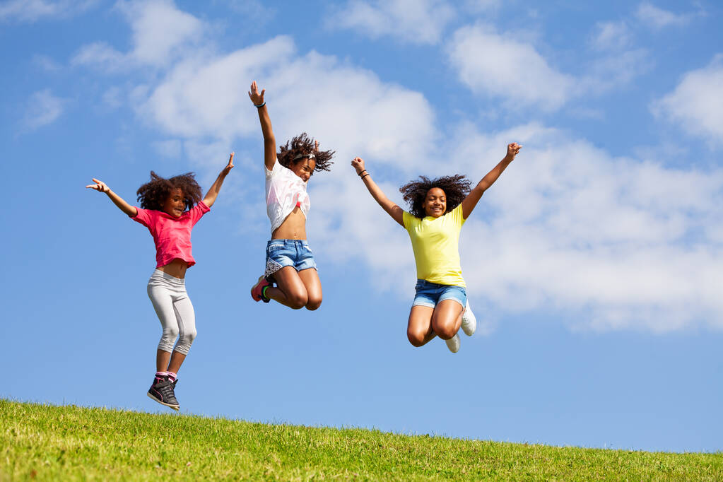 Groep drie springen hoge meisjes over schone blauwe hemel met opgeheven handen blije gezichten en vliegend haar - Foto, afbeelding