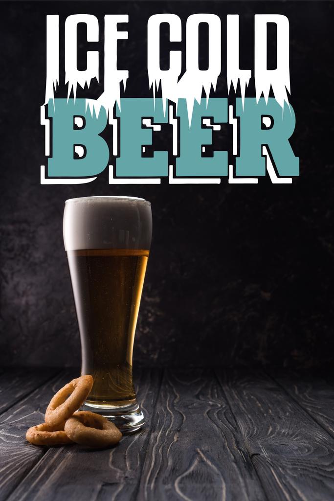 冷たいビールのレタリングと木製のテーブルの上に揚げ玉ねぎリングの近くの新鮮な軽ビールのガラス - 写真・画像