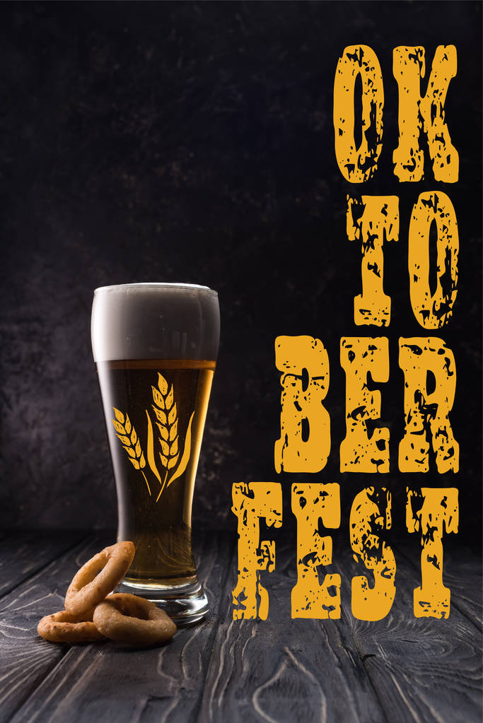 Kızarmış soğan halkalarının yanında bir bardak taze bira, ahşap masa üzerinde sarı oktobira festivali harfleriyle. - Fotoğraf, Görsel