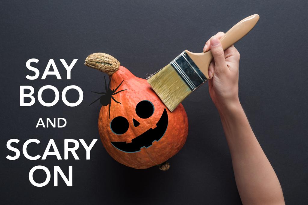 partial view of woman holding paintbrush near pumpkin on black background with say boo and scary on illustration - Photo, Image