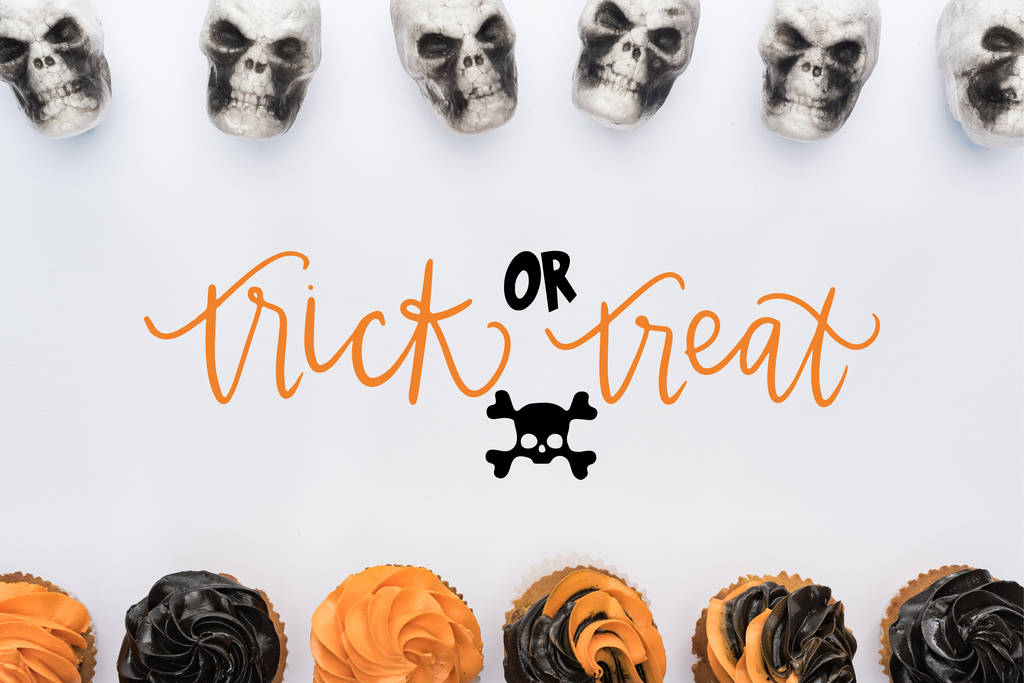верхний вид вкусные кексы Хэллоуин и черепа на белом фоне с трюком или лечения иллюстрации
 - Фото, изображение