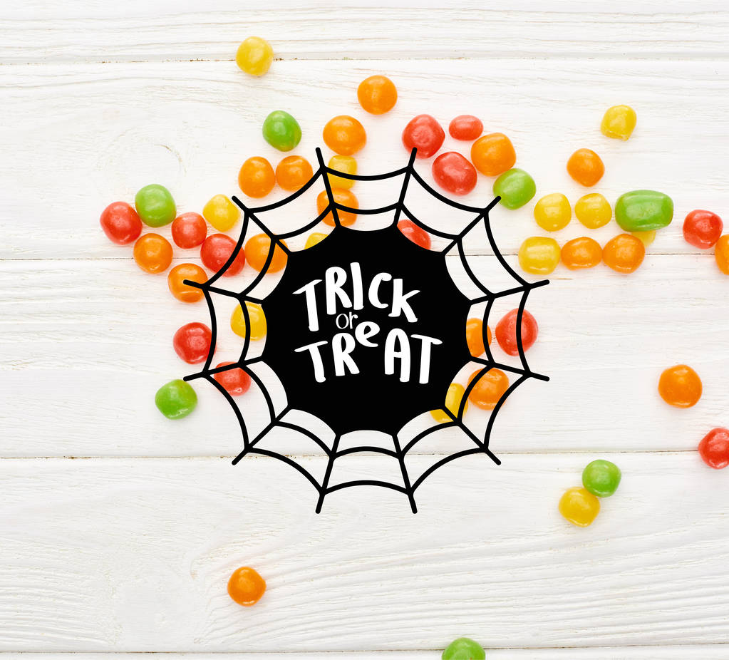 top view of colorful bonbons on white wooden table with spiderweb and trick or treat illustration - Photo, Image
