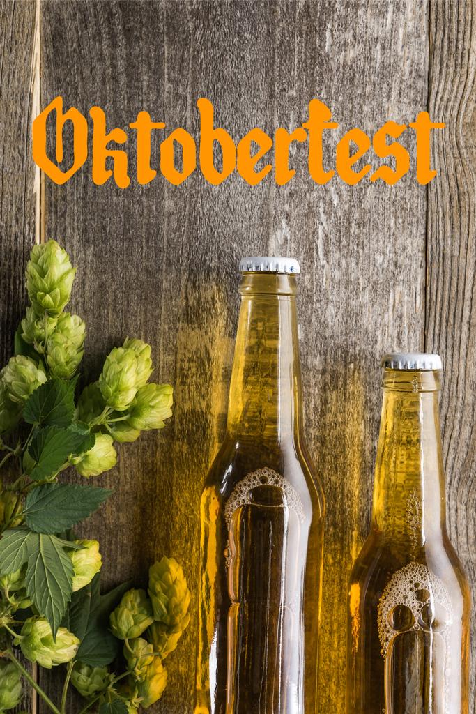 Draufsicht auf frisches Bier in Flaschen mit grünem Hopfen auf Holzoberfläche mit Oktoberfest-Schriftzug - Foto, Bild