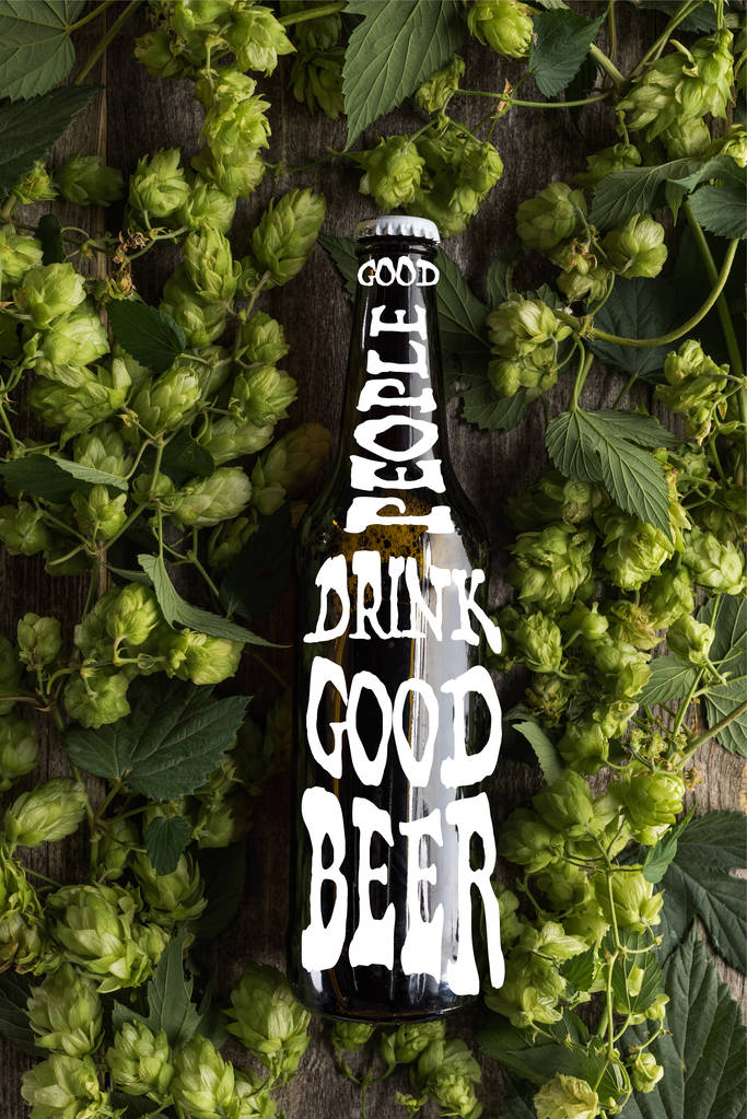 Draufsicht auf frisches Bier in Flasche mit guten Menschen trinken gutes Bier Schriftzug in grünem Hopfen auf Holzoberfläche - Foto, Bild