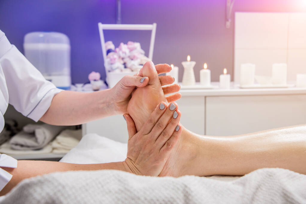 Mooie jonge vrouw geniet van voetmassage in spa salon. Cosmetologisch concept - Foto, afbeelding