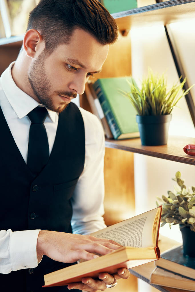 Hezký mladý muž v elegantním obleku čte knihu v moderním luxusním interiéru. Koncept hobby - Fotografie, Obrázek