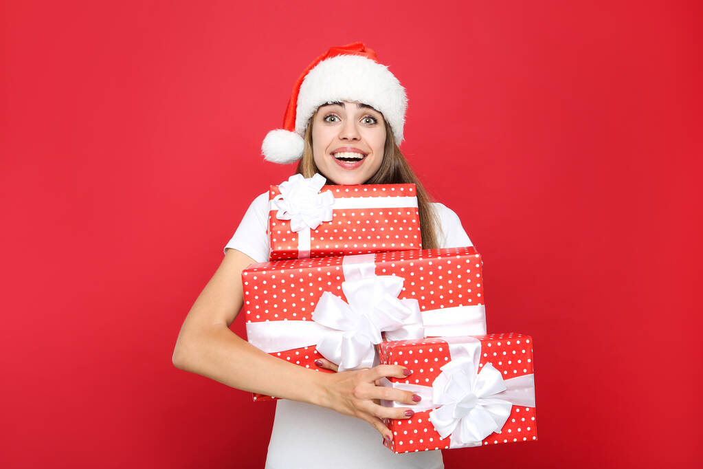 Bella donna che indossa il cappello di Babbo Natale e che tiene scatole regalo sul rosso
  - Foto, immagini