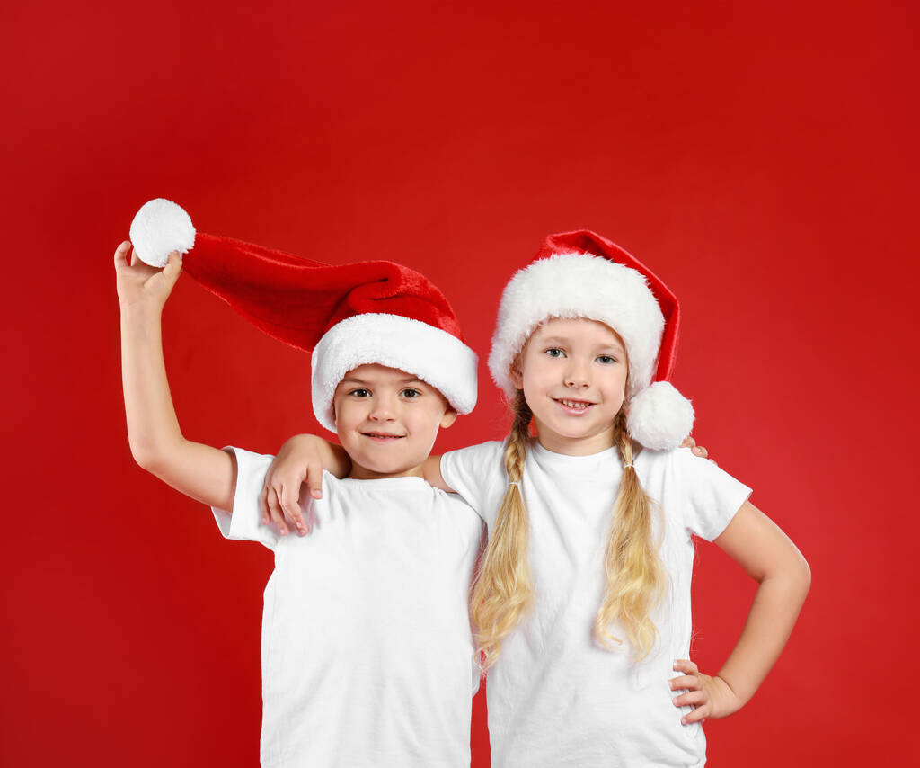 Χαριτωμένα παιδάκια που φοράνε καπέλα Αϊ-Βασίλη σε κόκκινο φόντο. Χριστουγεννιάτικες διακοπές - Φωτογραφία, εικόνα