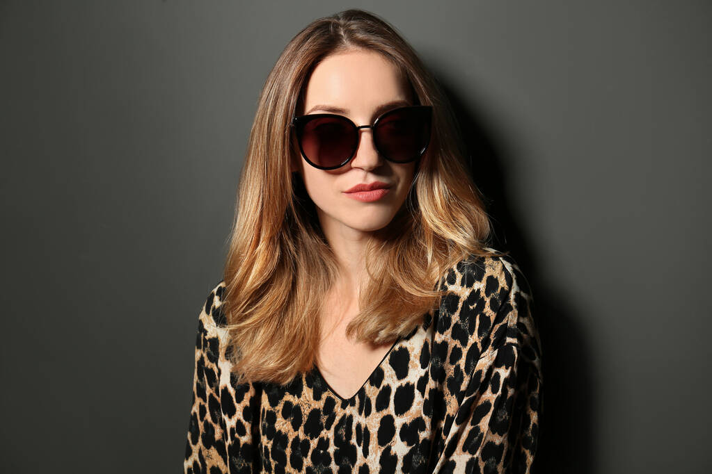 junge Frau mit stylischer Sonnenbrille auf dunkelgrauem Hintergrund - Foto, Bild