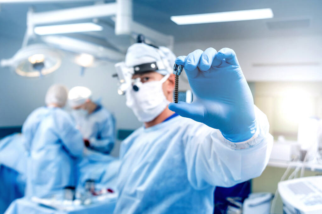 Chirurgia spinale. Il chirurgo mostra una vite poliassiale in sala operatoria con attrezzature chirurgiche. Laminectomia. Sistemi di fissazione della colonna vertebrale. Contesto medico
 - Foto, immagini