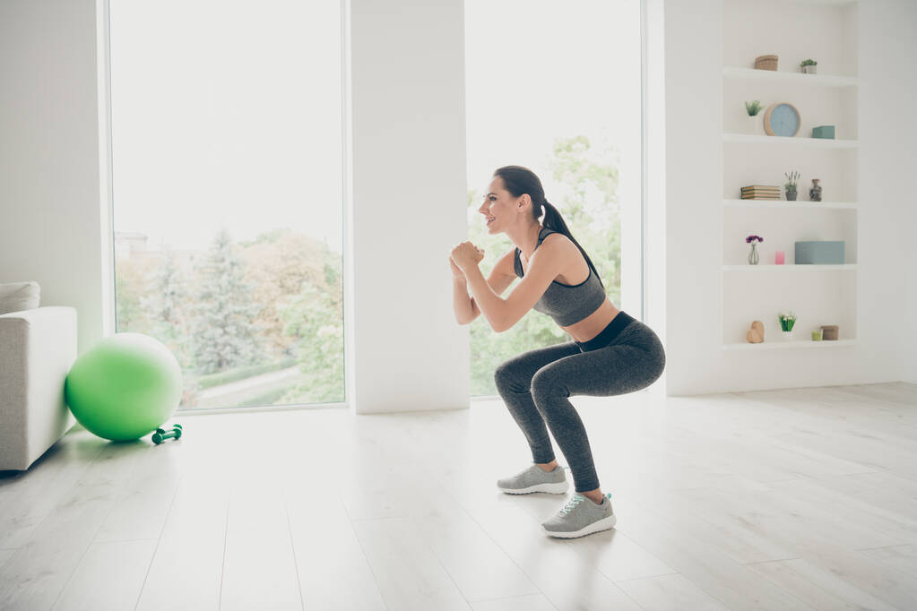 Pełnowymiarowe zdjęcie boczne radosne zwinność kochanek dziewczyna robi sport jogi ćwiczenia siedzieć przysiady ćwiczenia pilates aerobik nosić nowoczesne spodnie trampki w domu jak studio fitness - Zdjęcie, obraz