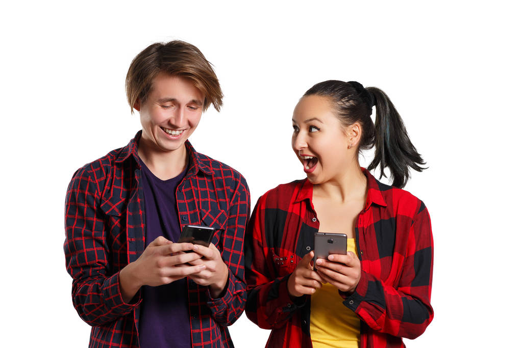 Feliz chico y chica joven con teléfonos inteligentes en la mano, charlando entre sí y riendo. aislado en blanco
 - Foto, Imagen