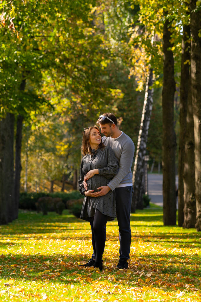 Молодая пара с беременной женой стоит в парке
 - Фото, изображение