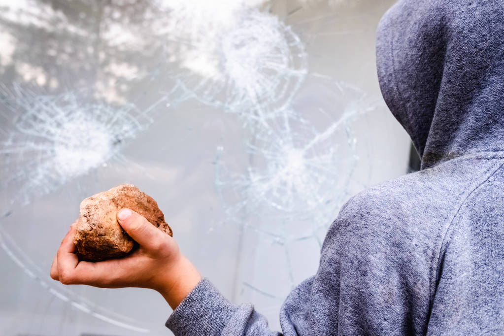 Criança segura uma pedra para jogá-lo contra um copo e quebrar um vento
 - Foto, Imagem